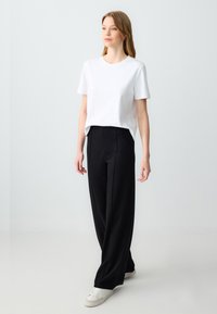 T-shirt blanc à manches courtes avec un col rond, associé à un pantalon large noir. Le pantalon présente une texture lisse et des coutures discrètes.