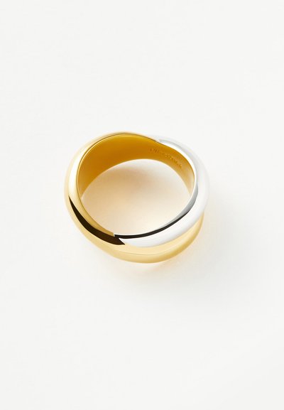 Δαχτυλίδια από χρυσό και ασήμι συνδεδεμένα σχηματίζοντας έναν συνεχόμενο βρόχο σε λευκό φόντο, τονίζοντας την αντίθεση μεταξύ των δύο μετάλλων.