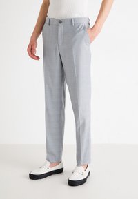 Pantaloni grigi chiari su misura con un delicato motivo a quadri, in tessuto leggero, taglio dritto e tasche frontali, abbinati a scarpe bianche slip-on.