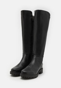 Botas negras hasta la rodilla de cuero suave, con cremallera frontal, suela de goma gruesa y punta ligeramente redondeada.