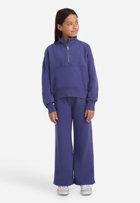 Suéter de forro polar púrpura con cuello de media cremallera y puños acanalados, combinado con pantalones anchos a juego. Textura suave, ajuste casual.