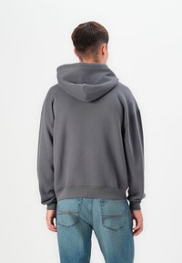 Grey hooded sweatshirt with a relaxed fit, ribbed cuffs and hem, made from soft fabric. Worn with light blue jeans.