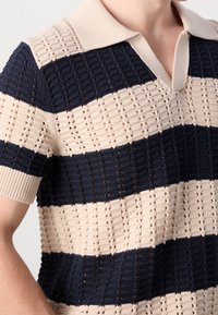 Pletená polokošile v béžových a námořnicky modrých pruzích, krátké rukávy, texturovaný vzor s otevřeným pleteným detailem a žebrovaný límec a manžety.