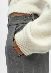 Graue Nadelstreifenhose mit Taschen, kombiniert mit einem cremefarbenen Strickpullover mit geripptem Bündchen. Nahaufnahme der Stofftextur.
