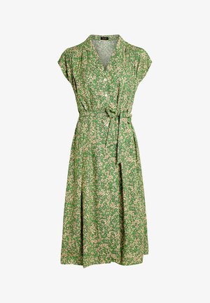 Groene wikkeljurk met een bloemenpatroon in beige. Korte mouwen, v-hals, en een gestrikt middel. Vloeiende stof met een lengte tot de knie.
