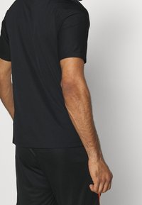 Maglietta atletica nera a maniche corte con un motivo testurizzato. Realizzata in materiale leggero. Design aderente con scollatura rotonda.