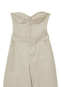 Combinaison beige avec un design sans bretelles, un corsage structuré et une fermeture éclair à l'arrière. Comprend des poches latérales et un tissu texturé.