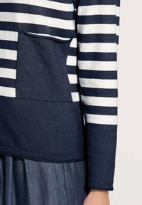 Langärmliges navy- und weißgestreiftes Hemd mit einfarbigem navy Tasche und Manschette, getragen über einem blauen plissierten Rock.