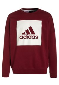 Sudadera burdeos con cuello redondo, que presenta un diseño cuadrado blanco y el logo "adidas" en burdeos en el centro. Tejido suave y texturizado.