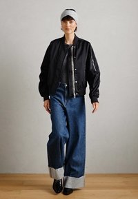 Black bomber jacket, gray knit top, wide-leg blue jeans with cuffed hems, and black ankle boots. Accessories include a gray headband.
