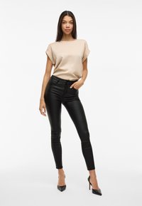 Béžová blůza s krátkým rukávem, kterou doplňují černé skinny kalhoty z umělé kůže a černé lodičky se špičatou špičkou, představující minimalistický design.