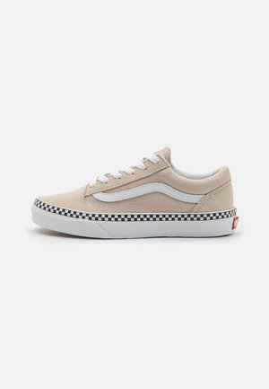 Lav profil beige sneaker med hvide snørebånd, hvid sidestribe og sort-hvid ternet mønster over den hvide sål.