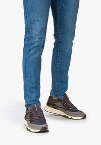 Sneakers sportivi caratterizzati da un mix di materiali grigio scuro con una tomaia in rete testurizzata e una suola imbottita, abbinati a jeans slim blu.