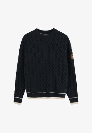 Granatowy sweter z plecionki z okrągłym dekoltem, kontrastującymi kremowymi i granatowymi ściągaczami na mankietach i u dołu, z naszywką na lewym rękawie.