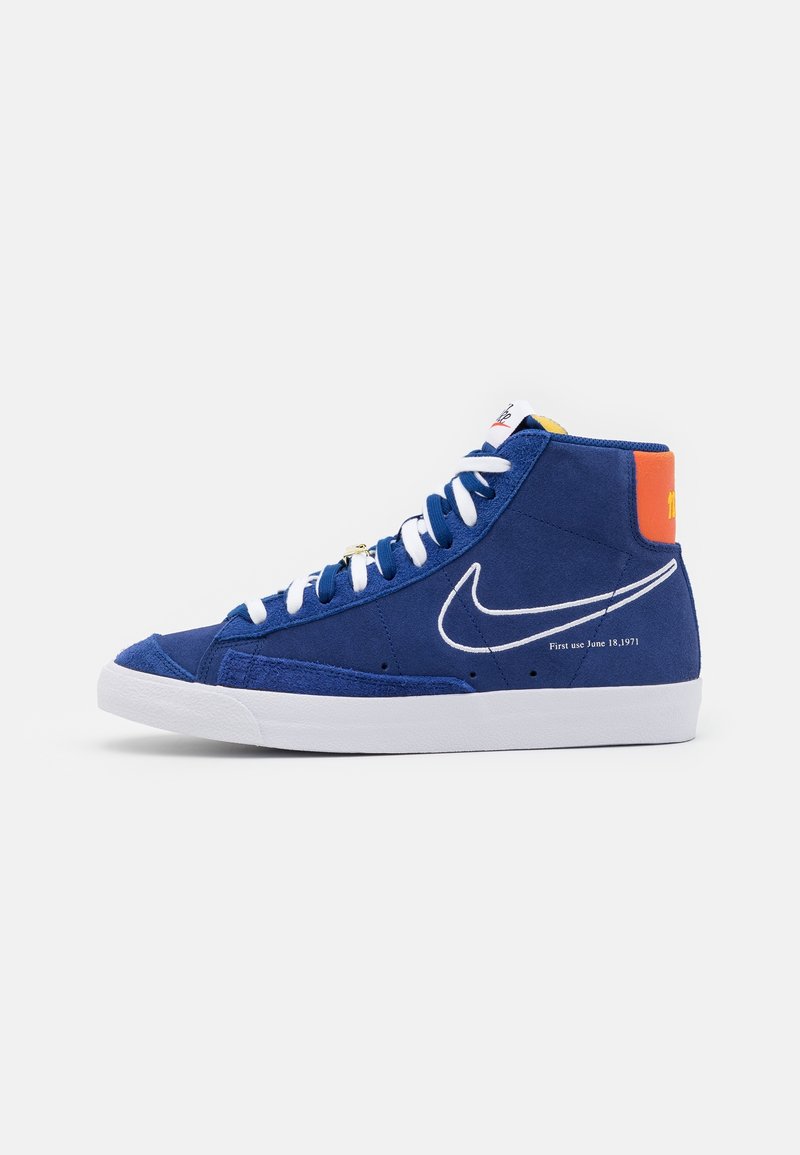 High-top sneaker in blue suede with white accents, featuring a white Nike logo, orange heel tab, and text "First use June 18, 1971."