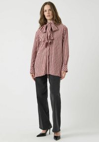 Rood-witte geblokte blouse met een strik rond de hals, gecombineerd met donkergrijze recht-toe recht-aan jeans en zwarte puntige hakken.