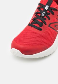 Czerwony obuwie sportowe z przewiewną siateczką, czarnymi sznurówkami i teksturowaną podeszwą; posiada białą podeszwę środkową z widocznym logo.