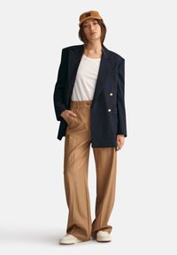 Marinblå dubbelknäppt kavaj, vit t-shirt, beige högmidjade byxor, krämfärgade sneakers och en kordfluga keps med logotypapplikation.
