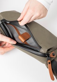 Olijfgroene tas met een zwarte rits en bruine leren accenten. Interne gaasvak zichtbaar, met een zachte stoffen voering.