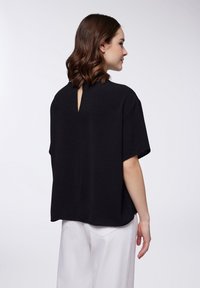 Top corto nero a maniche corte con finitura testurizzata e dettaglio con apertura a goccia sulla schiena, caratterizzato da una vestibilità ampia e un sottile design con spalle scese.