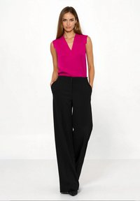 Fuksjowy top bez rękawów z dekoltem w serek, zestawiony z wysokim stanem czarnymi szerokimi spodniami z bocznymi kieszeniami i zapięciem na guziki.