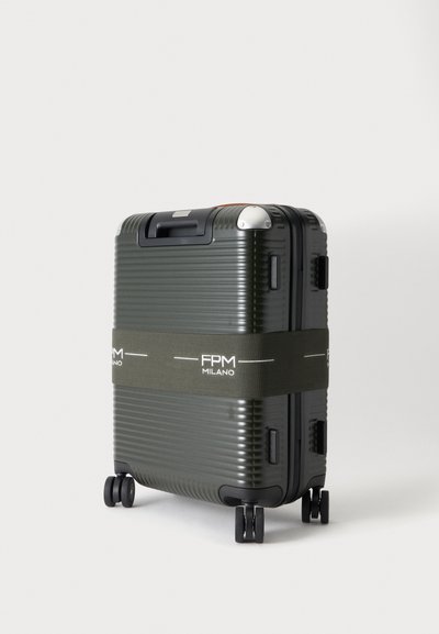 Valise rigide vert foncé avec quatre roues et une sangle vert olive étiquetée FPM Milano autour de son milieu.