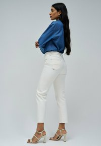 Jeans blancos de talle alto combinados con una camisa de denim azul y tacones de tiras beige. El conjunto presenta líneas limpias y una silueta ajustada.
