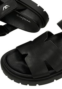 Czarne sandały z otwartym palcem wykonane ze skóry, wyposażone w grube podeszwy i wycięcia, z regulowanymi paskami oraz teksturowaną wkładką zapewniającą komfort.