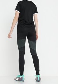 Leggings sportivi neri con motivi a pois testurizzati, abbinati a una t-shirt nera con dettagli bianchi e scarpe da ginnastica grigie con lacci turchesi.