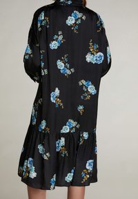 Robe noire à motifs floraux avec de grandes roses bleues et un feuillage vert. Fabriquée en tissu doux avec un ourlet en couches et des manches amples.
