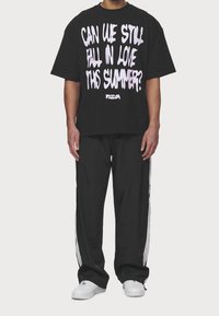 Svart oversized t-shirt med vitt och rosa grafiskt text. Matchas med svarta byxor med vita sidostycken och vita sneakers.