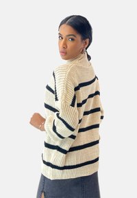 Stickad polotröja i krämfärgad med svarta horisontella ränder. Mysig textur och lös passform, med ribbade detaljer vid fåll och ärmslut.