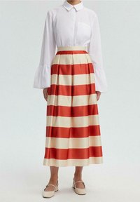 Chemisier blanc à col avec de larges manches évasées, associé à une longue jupe plissée aux larges bandes horizontales rouges et crème.