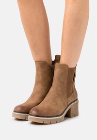 Braune, kunstlederne Stiefeletten mit einem dicken Absatz, elastischen Seitenpanels und einem Reißverschluss, ausgestattet mit einer strukturierten Oberfläche und einer stabilen Sohle.