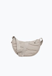 Lyse beige quilttet halvmåne crossbody taske med justerbar bred rem og lynlåslukning på en ensfarvet baggrund.