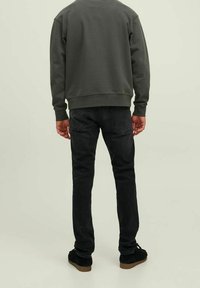 Sudadera gris oscuro con cuello redondo, combinada con jeans negros ajustados. El calzado presenta zapatos de ante oscuros con una suela marrón clara.