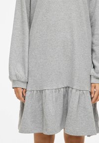 Robe grise à manches longues en tissu doux, avec un ourlet à volants et des poignets ajustés. Le design est simple avec une silhouette décontractée.