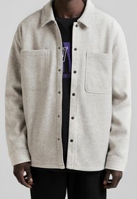 Jasnoszara kurtka z mieszanki wełny, z kołnierzem, zatrzaskami i dwoma przednimi kieszeniami; charakteryzuje się miękkim, teksturowanym wykończeniem.