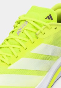 Felle gele Adidas hardloopschoen met witte strepen, neon gele veters en de tekst "ADIZERO" op de tong.