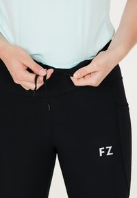 Svarta träningbyxor med dragsko i midjan, med den reflekterande "FZ"-logotypen och sidofickor. Slät textur, åtsittande design.