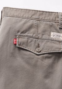 Taupe Levi's pants back pocket with buttoned flap and red Levi's tag, showing stitched seams and brand label.