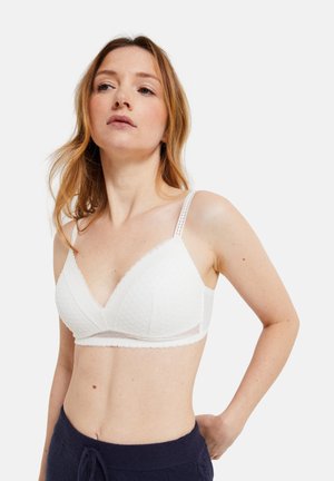 Bralette en triangle blanc en tissu texturé avec un motif à pois. Comprend des bretelles réglables et une bande en mesh transparent en dessous de la poitrine.