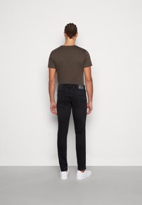 Černé džíny z denimu s přiléhavým střihem, spárované s tmavě hnědým tričkem s krátkým rukávem. Na zadním pásu je štítek. Bílé tenisky.