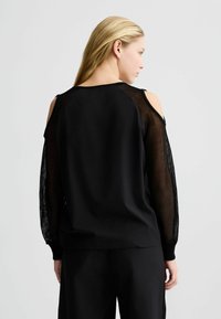 Czarny sweatshirt z siateczkowymi rękawami, wycięciami na zimne ramiona i ściągaczami. Gładka tekstura materiału, luźny krój, minimalistyczny design.