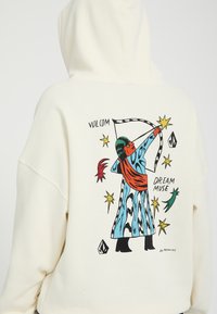 Sweat à capuche avec un graphisme coloré d’un archer en robe à motifs, entouré d’étoiles et du texte "Volcom" et "Dream Muse".