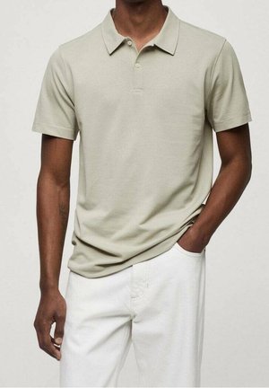 Polo shirt gris clair à manches courtes, avec col et trois boutons. Fabriqué en tissu lisse et extensible. Porté avec un pantalon blanc.