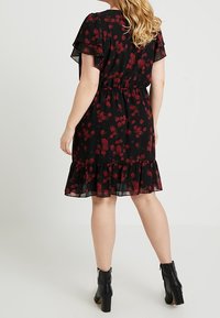 Svart blommig klänning med röda rosor, volangärmar, elastisk midja och en lager på lager volangslutning, tillsammans med svarta ankelstövlar.