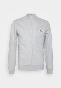 Chaqueta gris con cremallera hecha de una tela suave, con un cuello simulado, mangas largas y un pequeño logo verde en el pecho.