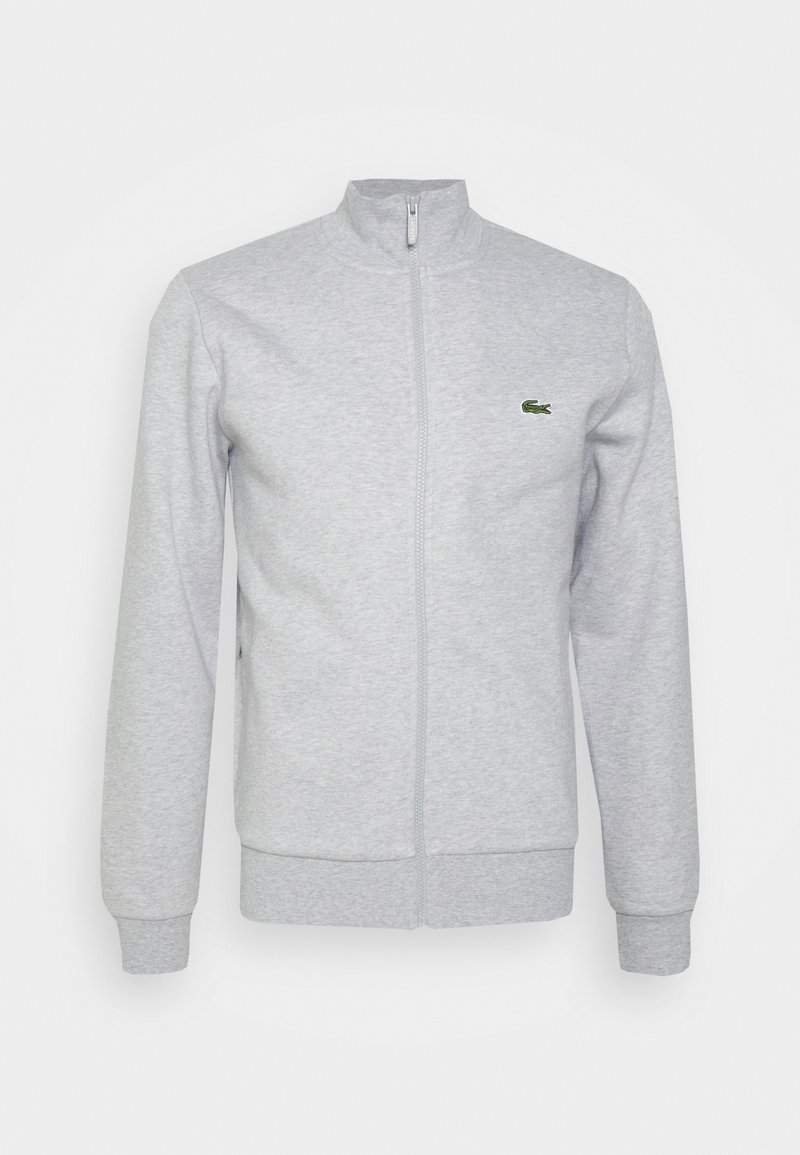 Chaqueta gris con cremallera hecha de una tela suave, con un cuello simulado, mangas largas y un pequeño logo verde en el pecho.