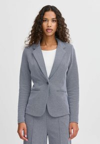 Grå stickad blazer med en notch lapel, enkel knappstängning och två framfickor. Texturerad tyg med en figursydd silhuett.